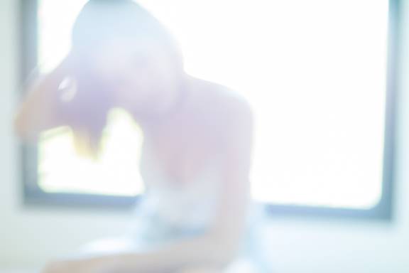 Defocused image of a person with a window behind them. The background is brightly lit, giving the image a soft, dreamy feel.